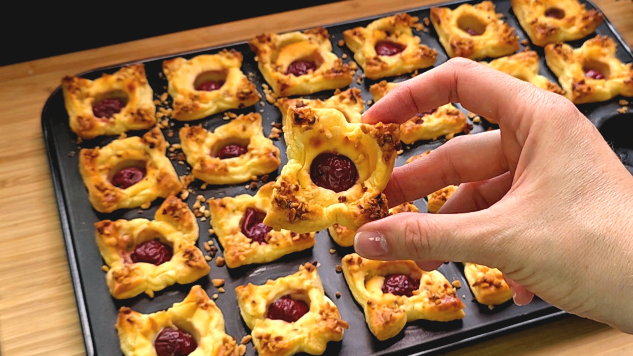 Detailansicht eines Mini-Muffins aus Blätterteig mit einer tiefroten Sauerkirsche in cremiger Quarkfüllung und krossen Nüssen.