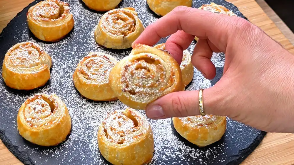 Detailansicht einer frisch gebackenen Blätterteigschnecke mit sichtbaren, saftigen Apfelraspeln und karamellisiertem Zimt-Zucker.