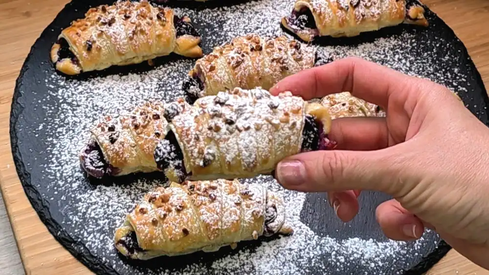 Detailansicht eines frisch gebackenen Croissants mit prallen, heißen Heidelbeeren in saftiger Quarkcreme und gerösteten Nüssen.