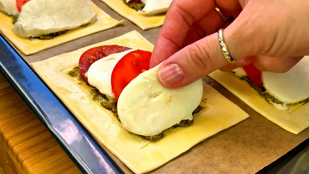 Detailansicht eines frisch gebackenen Tomate-Mozzarella-Blätterteigs mit Blasen schlagendem Käse und grünem Pesto.