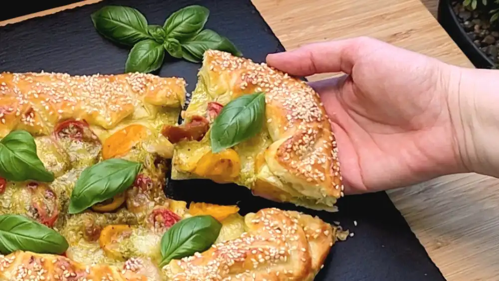 Detailansicht der rustikalen Galette mit geschmolzenem Käse, saftigen Tomaten und goldgelbem Sesamrand.