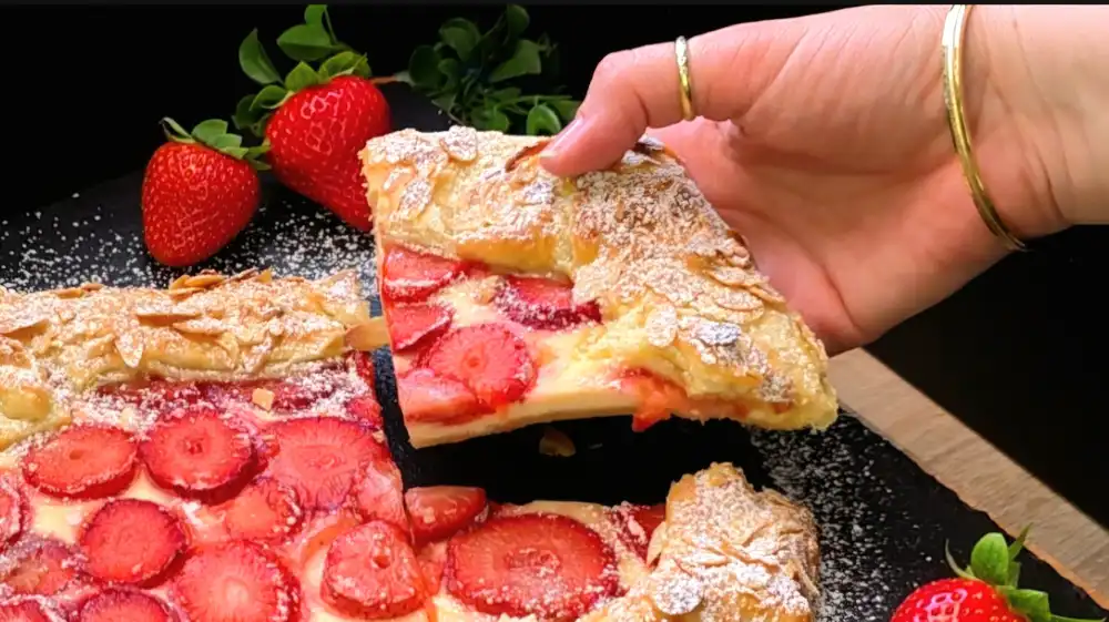 Detailansicht der glänzenden Erdbeerfüllung und der gerösteten Mandelblättchen auf dem Teigrand.