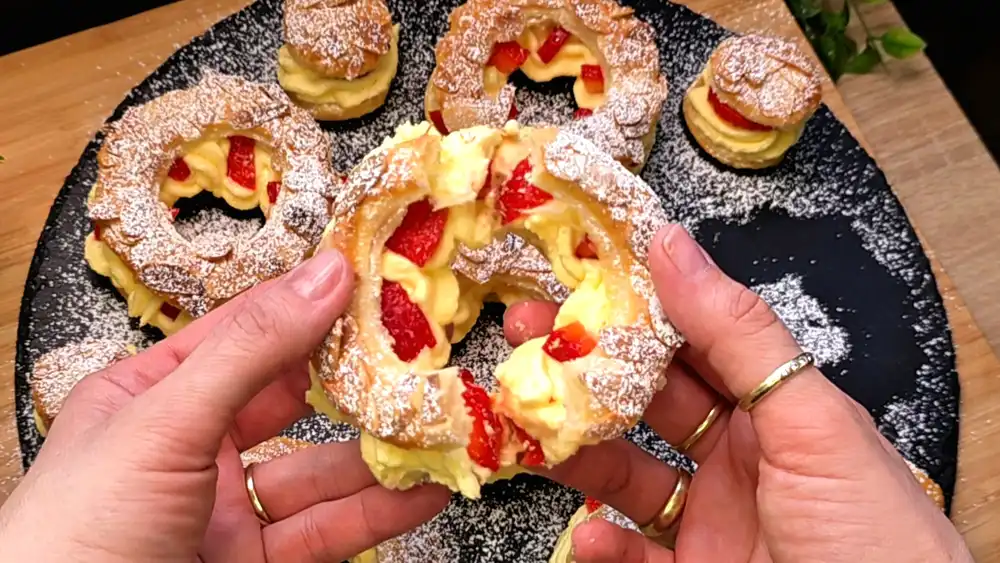 Detailansicht eines aufgeschnittenen Blätterteigrings mit wellenartig aufgespritzter Paradies-Creme, saftig roten Erdbeerstücken und röstigen Mandeln.