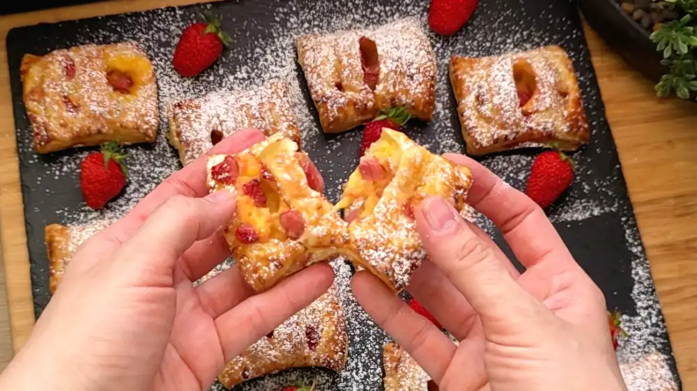 Detailansicht einer gebackenen Blätterteigtasche mit dekorativem Gabelrand und gelbem Puddingkern mit Erdbeeren.