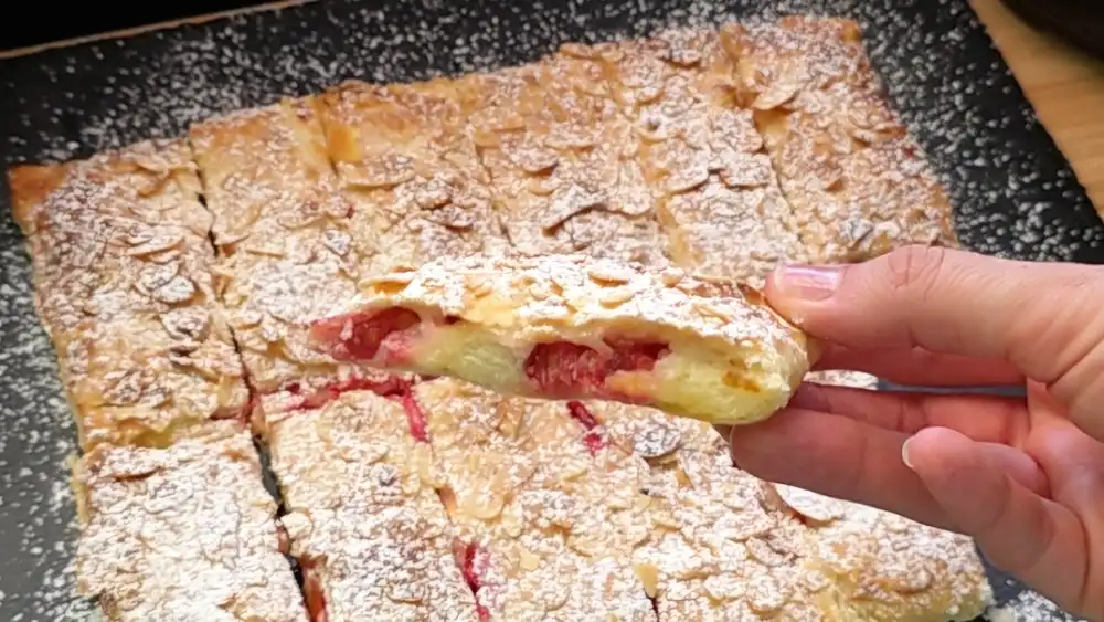 Detailansicht eines aufgeschnittenen Blätterteig-Riegels, bei dem die cremige Vanille-Quark-Füllung und die prallen roten Beeren unter der knusprigen Mandelkruste zu sehen sind.