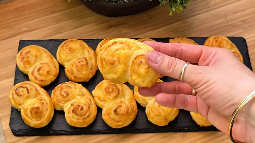 Detailansicht eines herzhaften Blätterteig-Öhrchens, das die perfekt gebräunten, blättrigen Schichten und den geschmolzenen Käse im Inneren zeigt.