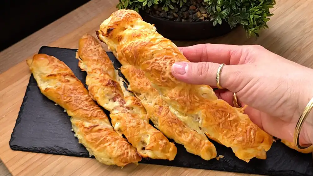 Detailansicht einer gedrehten Blätterteig-Stange, die den knusprigen Speck, den geschmolzenen Käse und die blättrigen Teigschichten zeigt.