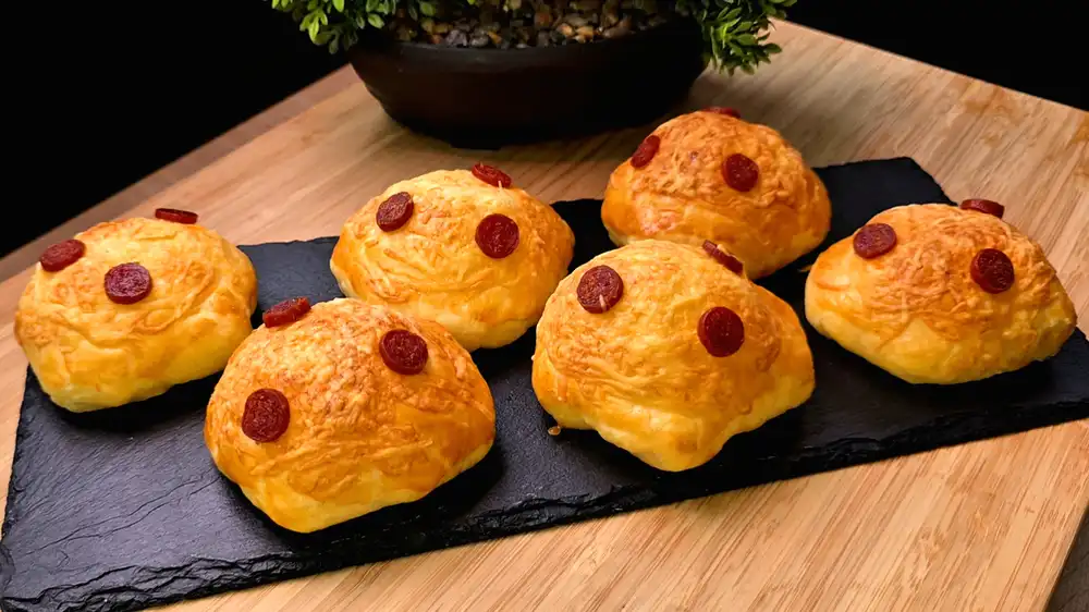 Goldbraun gebackene Blätterteig-Käse-Taschen mit einer knusprigen Kruste aus geschmolzenem Käse und Mini-Salami-Scheiben auf einem rustikalen Servierbrett.