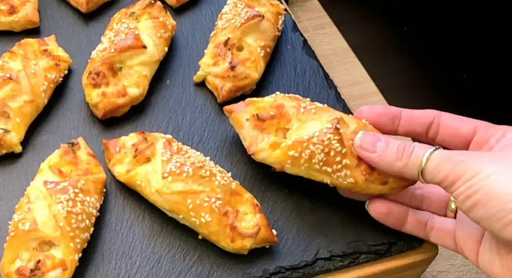 Detailansicht eines geöffneten Blätterteig-Schiffchens mit cremiger Frischkäse-Wurst-Füllung und geschmolzenem Käse.