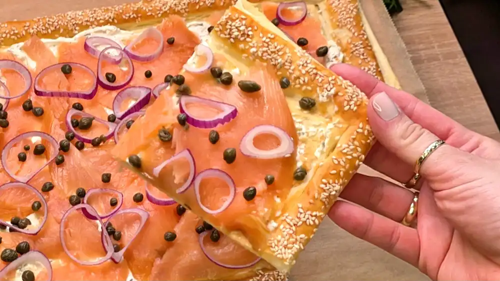 Detailansicht einer aufgeschnittenen Lachs-Tarte mit cremigem Kräuterfrischkäse, zartem Räucherlachs und feinen Kapern auf krossem Blätterteig.