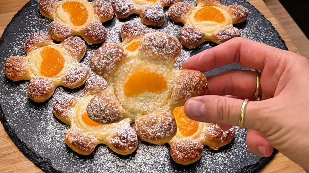 Detailansicht einer Blätterteig-Blume mit der goldgelben Vanille-Quarkcreme und einer saftigen Mandarinenscheibe im Zentrum.