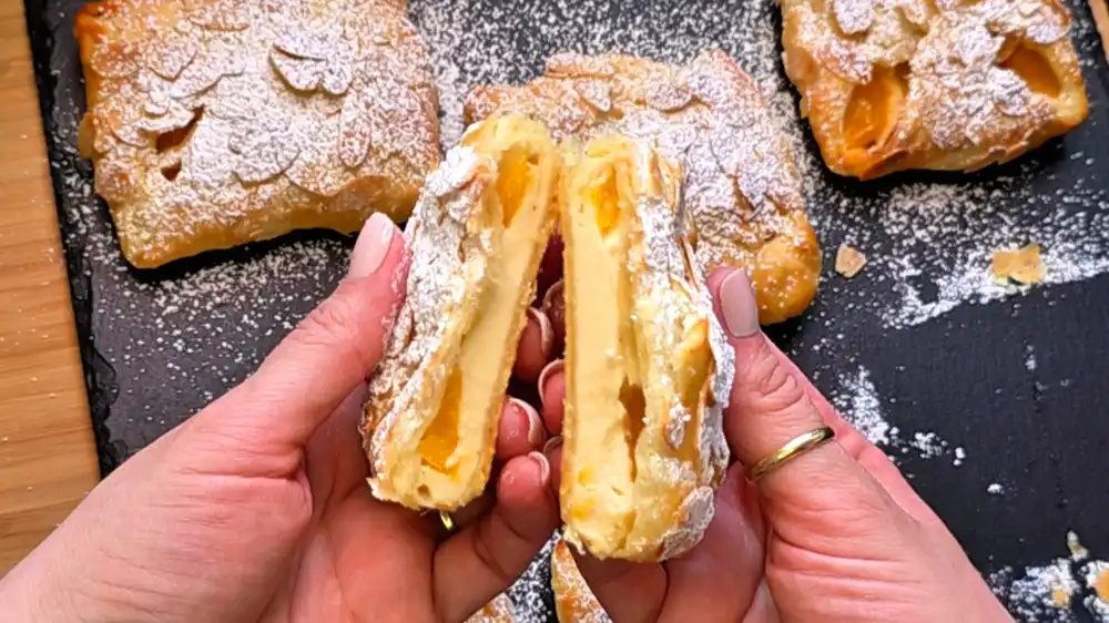 Detailansicht einer frisch gebackenen Pfirsichtasche mit geschmolzener Quarkcreme, saftigen Pfirsichwürfeln und gerösteten Mandeln.