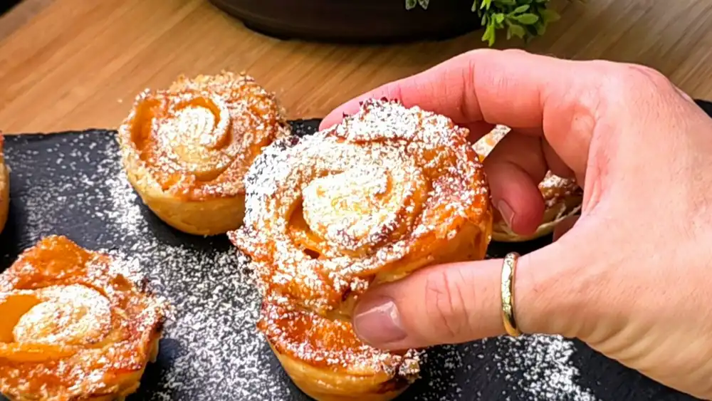 Detailansicht einer fertigen Blätterteig-Blüte, bei der die karamellisierten Pfirsichränder wie Rosenblätter aus den krossen Teigschichten ragen.