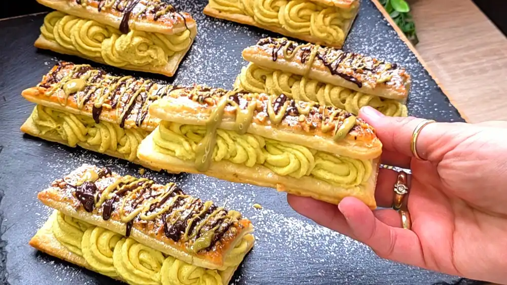 Detailansicht einer aufgeschnittenen Blätterteig-Schnitte mit herrlich grüner Pistazien-Sahnecreme und knackig gerösteten Pistaziensplittern.