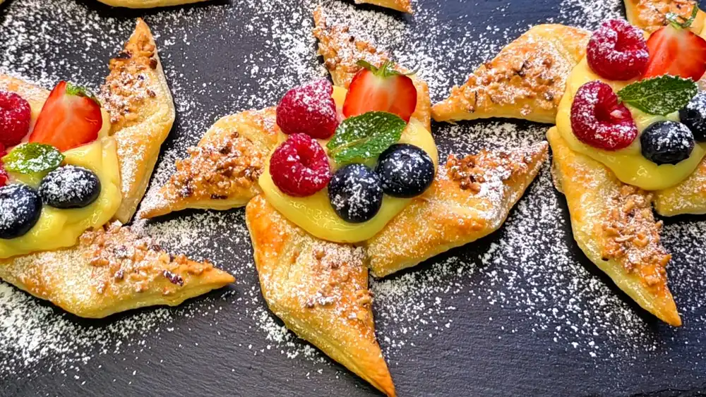 Detailansicht eines frisch gebackenen Pudding-Sternchens mit glänzendem Vanillekern, frischen Erdbeeren, Blaubeeren und gerösteten Nüssen.