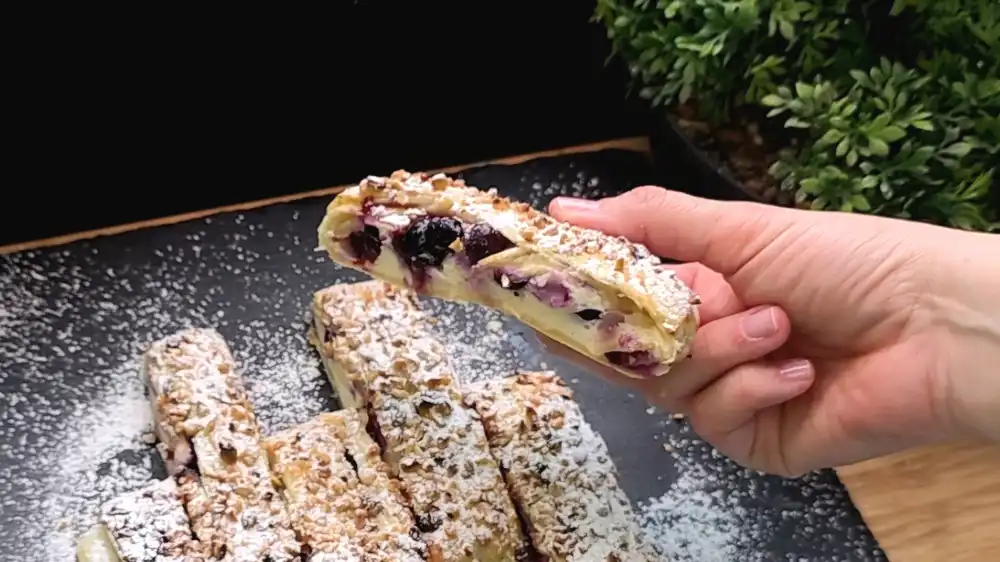 Detailansicht eines angeschnittenen Strudelstücks, bei dem die dicke, weiße Quark-Vanille-Schicht und die saftigen, tiefblauen Heidelbeeren im Inneren perfekt zu sehen sind.