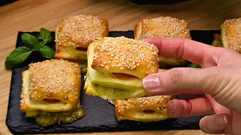 Detailansicht einer aufgeschnittenen Blätterteigtasche, bei der das grüne Pesto, die würzigen Salamischeiben und der fädenziehende Mozzarella im Inneren perfekt zu sehen sind.