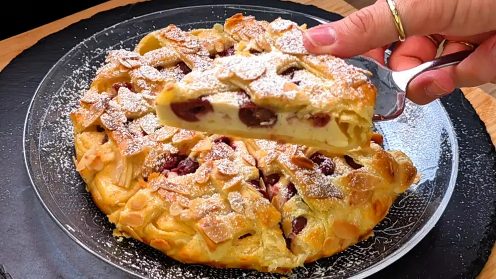 Detailansicht eines abgeschnittenen Stücks Kuchen, bei dem die dicke Vanille-Quark-Schicht und die saftigen Sauerkirschen unter dem knusprigen Gitter und den gerösteten Mandeln im Fokus stehen.