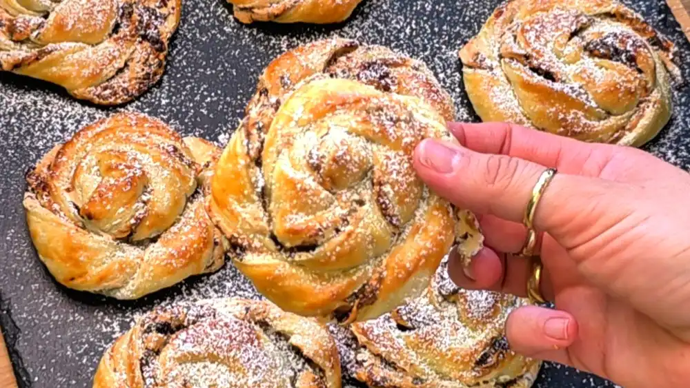 Detailansicht einer aufgebrochenen Blätterteigschnecke mit krossen Teigschichten und dem fluffigen, geschmolzenen Schokoladen-Schaum-Kern.