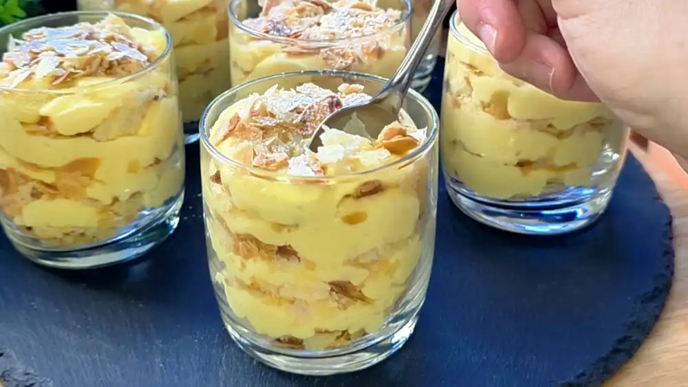 Detailansicht eines Dessertglases, das die kontrastreichen Schichten aus fluffig-samtiger Vanillecreme und den goldbraun gerösteten, krossen Mandel-Blätterteig-Crumbles perfekt zeigt.
