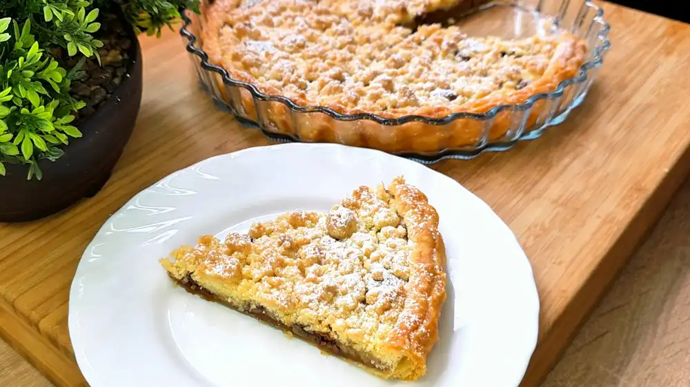 Detailansicht eines Kuchenschnitts mit sichtbaren Schichten aus geschmolzener Milchschokolade, Bananenscheiben, Biscoff-Kekscreme und krossem Teig.