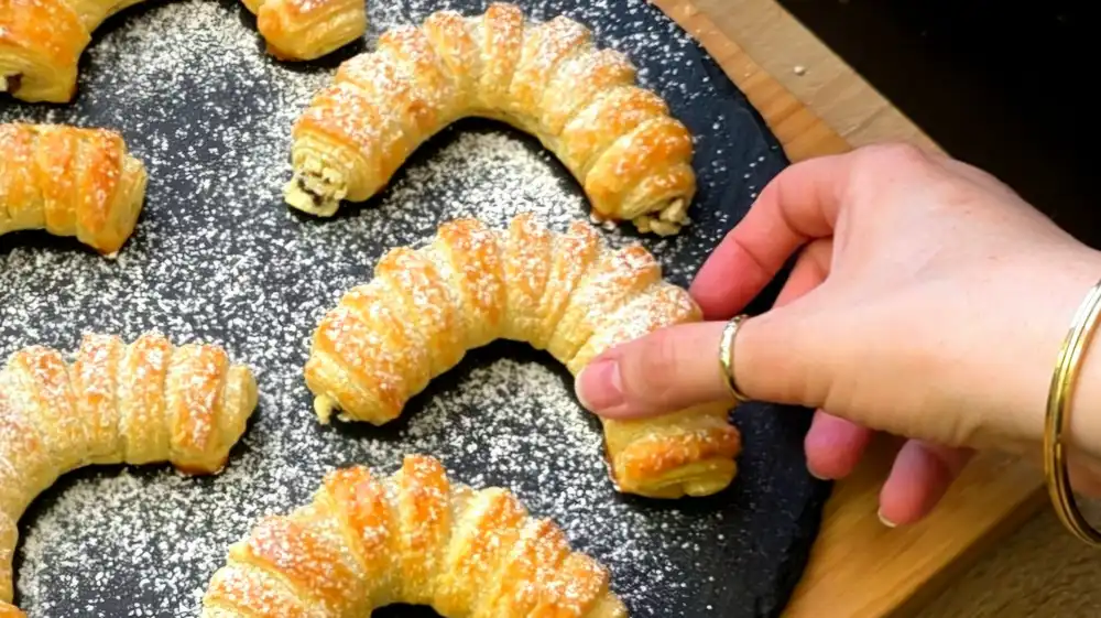 Detailansicht eines frisch gebackenen Schokoladenkipferls mit schmelzenden Schokoladentropfen und krossen Teigschichten.