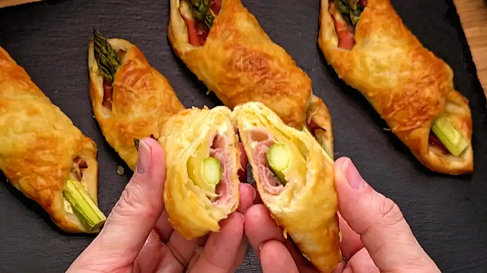 Detailansicht einer aufgeschnittenen Blätterteigtasche mit grünem Spargel, Schinken und Frischkäse.