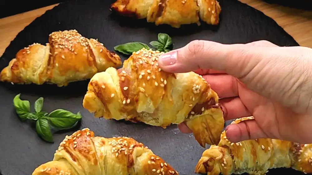 Detailansicht eines frisch gebackenen, krossen Blätterteig-Croissants, bei dem der knusprige Speck und der geschmolzene Käse an den Seiten herausragen.