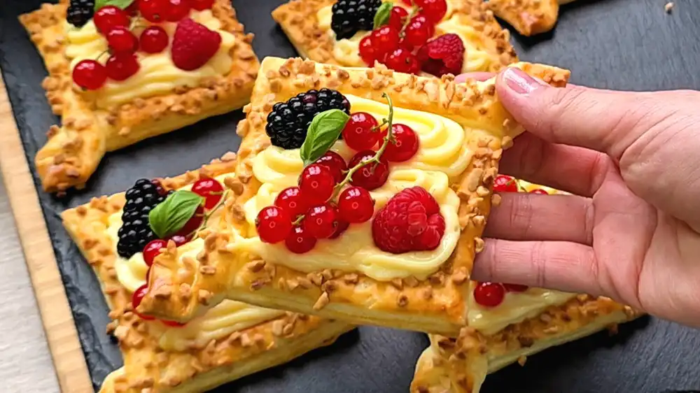 Detailansicht eines Blätterteig-Diamanten, bei dem der glänzende Vanillepudding und frische Beeren im Fokus stehen, umrahmt von kross gebackenen Mandelstücken.
