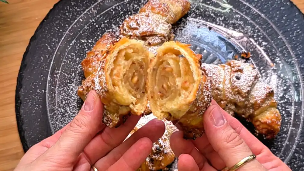 Detailansicht eines frisch gebackenen Zimt-Croissants mit krosser Nusskruste und Puderzucker.