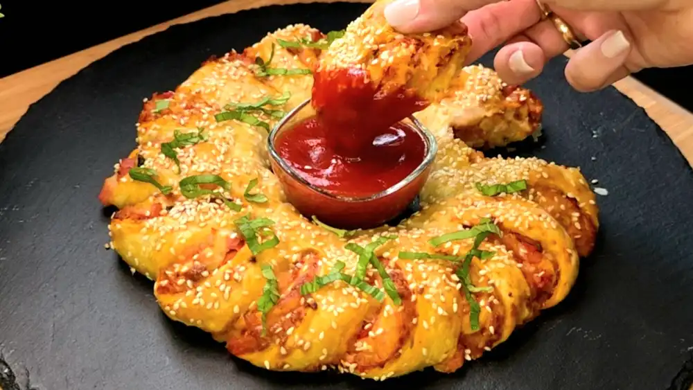 Goldbraun gebackener Blätterteig-Pizzakranz mit Schinken, Käse und einer Sesamkruste.