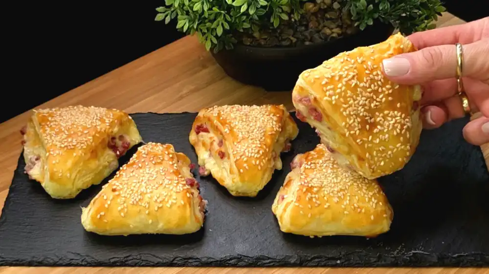 Goldbraun gebackene Schinken-Käse-Dreiecke aus Blätterteig mit goldgelber Sesamkruste.