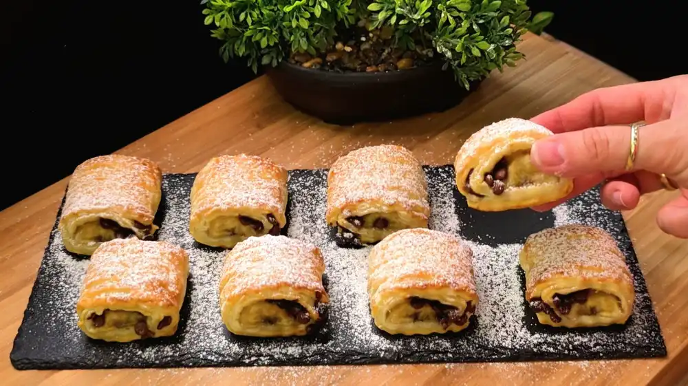 Goldbraun gebackene Schoko-Bananen-Häppchen aus Blätterteig, fein mit Puderzucker bestäubt.