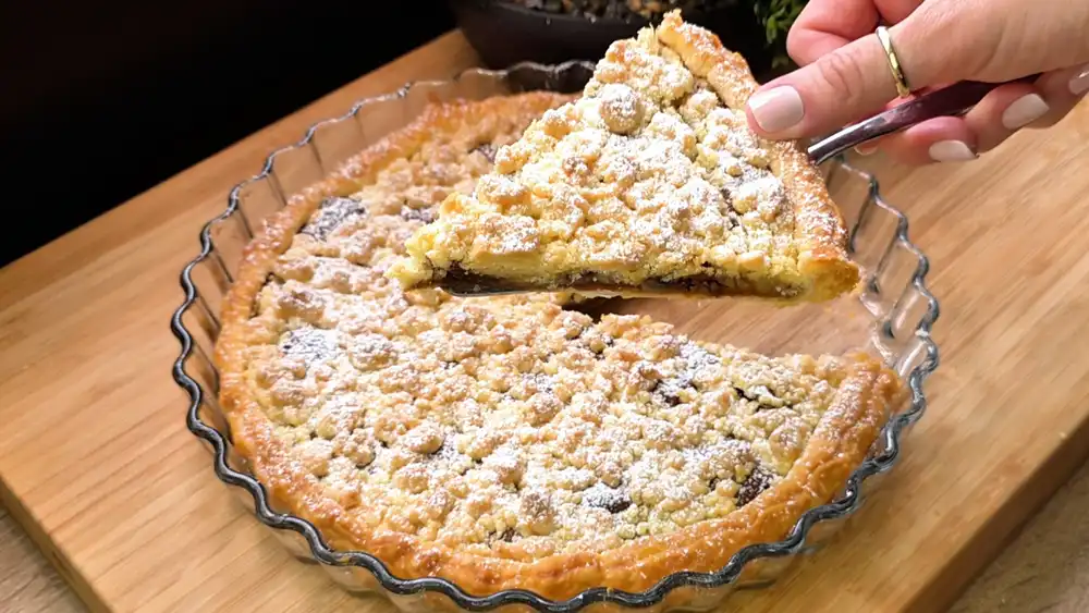 Ein frisch gebackener Schokoladen-Bananen-Kuchen aus Blätterteig in einer runden Glasform, bedeckt mit goldbraunen Streuseln und Puderzucker.