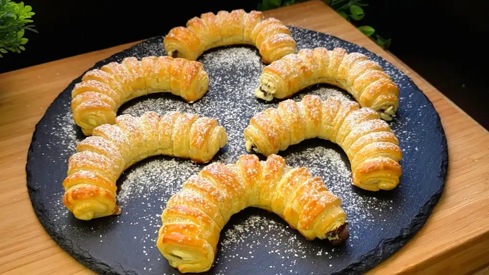 Goldbraun gebackene Blätterteig-Schokoladenkipferl mit feinem Streifenmuster und Puderzucker.
