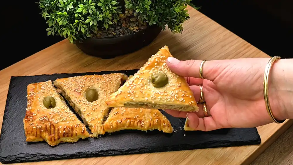Detailansicht eines aufgeschnittenen Thunfisch-Dreiecks mit saftiger Fisch-Zwiebel-Füllung und krossem Sesam-Blätterteig.
