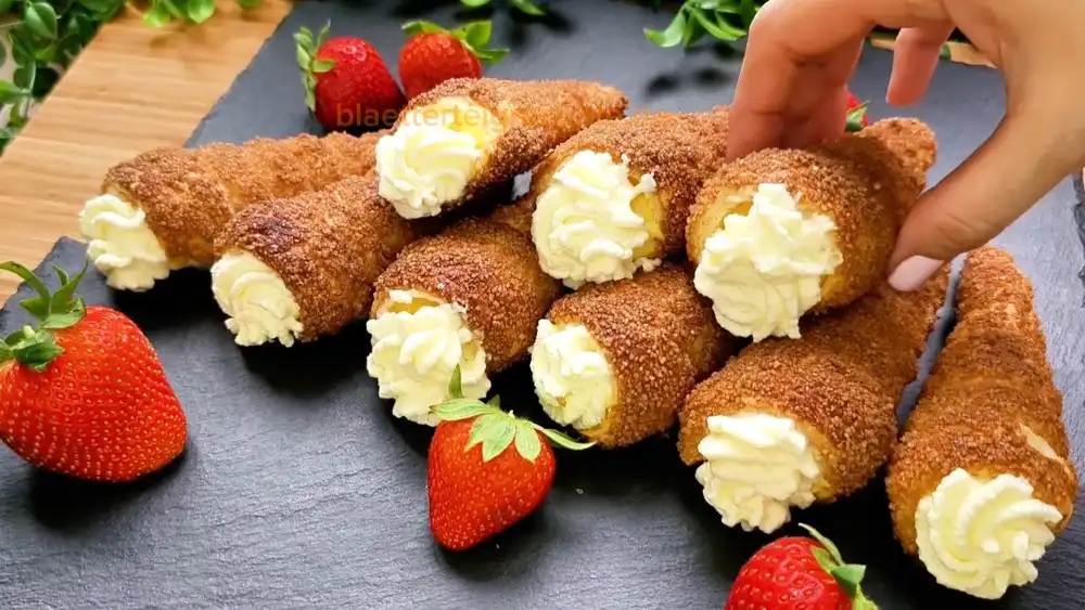 Goldbraun gebackene Blätterteig-Rollen mit einer karamellisierten Zimt-Zucker-Kruste, prall gefüllt mit cremiger Vanillefüllung und einem Sahnetupfer, auf einer eleganten Etagere.