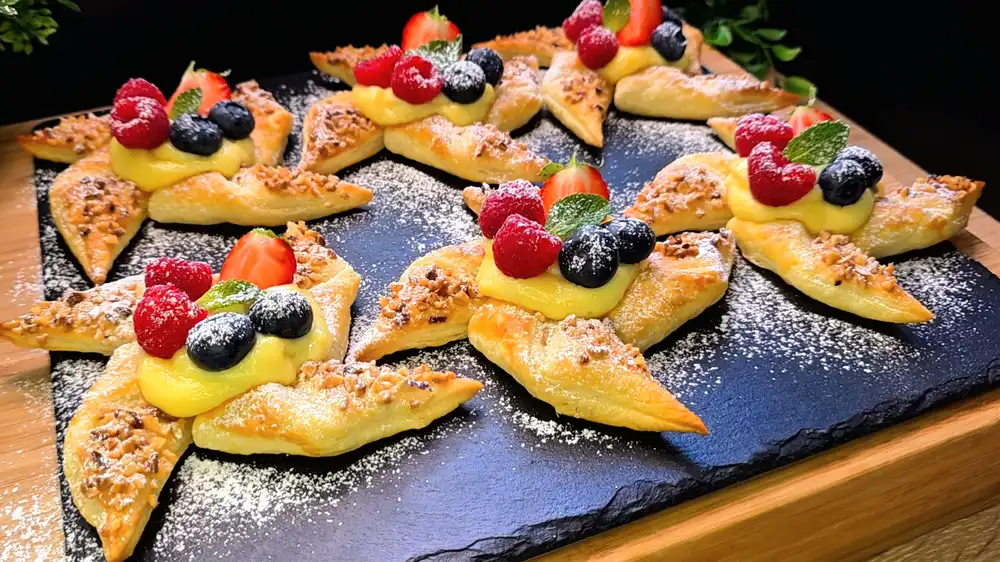 Goldbraun gebackene Blätterteig-Sternchen im Windrad-Design, gefüllt mit cremigem Vanillepudding und frischen Beeren.