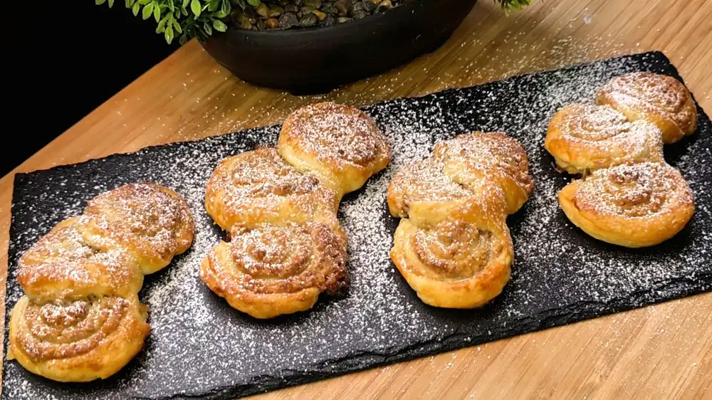 Goldbraun gebackene Walnussfächer aus Blätterteig mit kunstvoller Teigfaltung und einer feinen Puderzucker-Schneedecke.