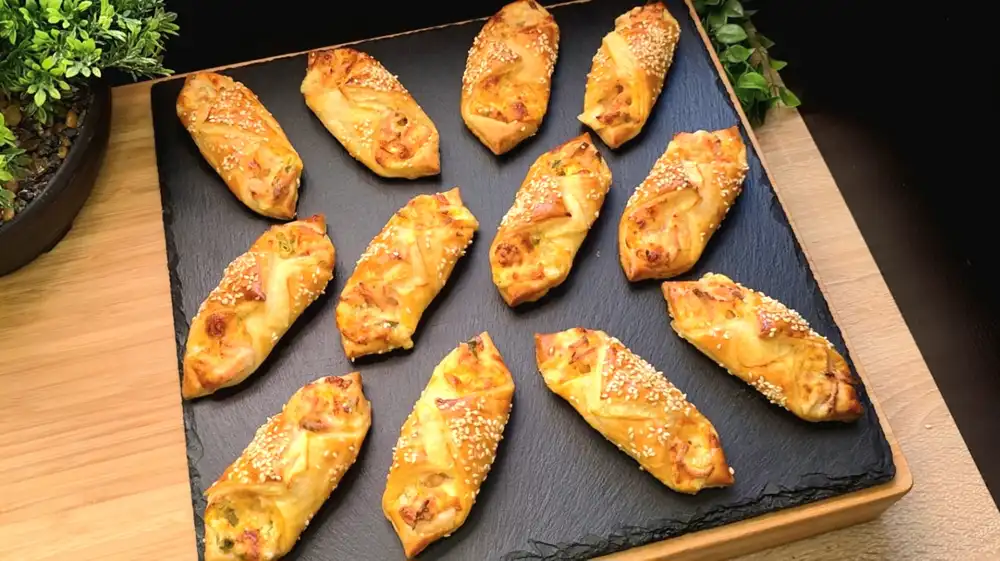Goldbraun gebackene Wurst-Käse-Schiffchen aus Blätterteig mit geschmolzenem Käse und Sesam.
