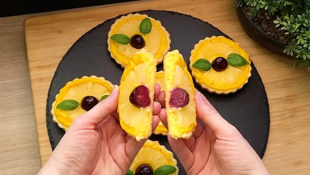 Detailansicht eines frisch gebackenen Ananas-Törtchens mit Fokus auf die cremige Vanillepudding-Schicht und die saftige Frucht im krossen Teigrand.