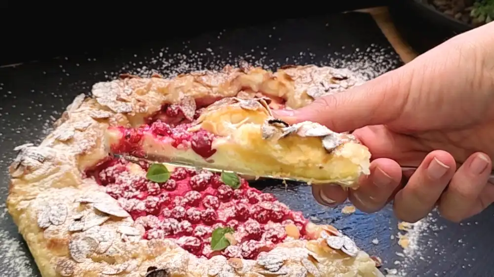 Detailansicht einer angeschnittenen Johannisbeer-Quark-Galette mit Fokus auf die samtige Vanillefüllung, die aufgeplatzten roten Beeren und den knusprigen Mandelrand.