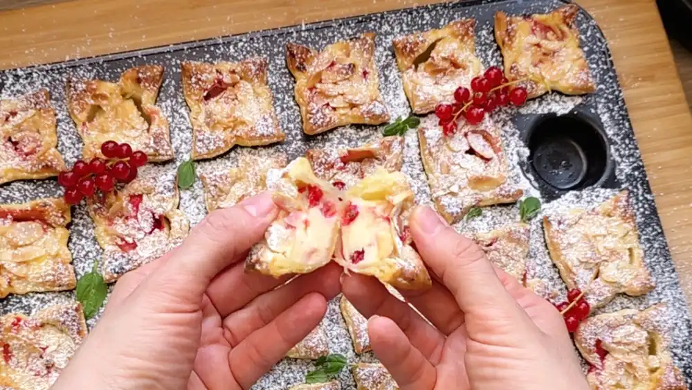 Detailansicht eines einzelnen Blätterteig-Mini-Muffins mit Fokus auf die cremige Vanille-Quark-Füllung, saftig eingebackene rote Beeren und die krossen Mandelplättchen am Rand.