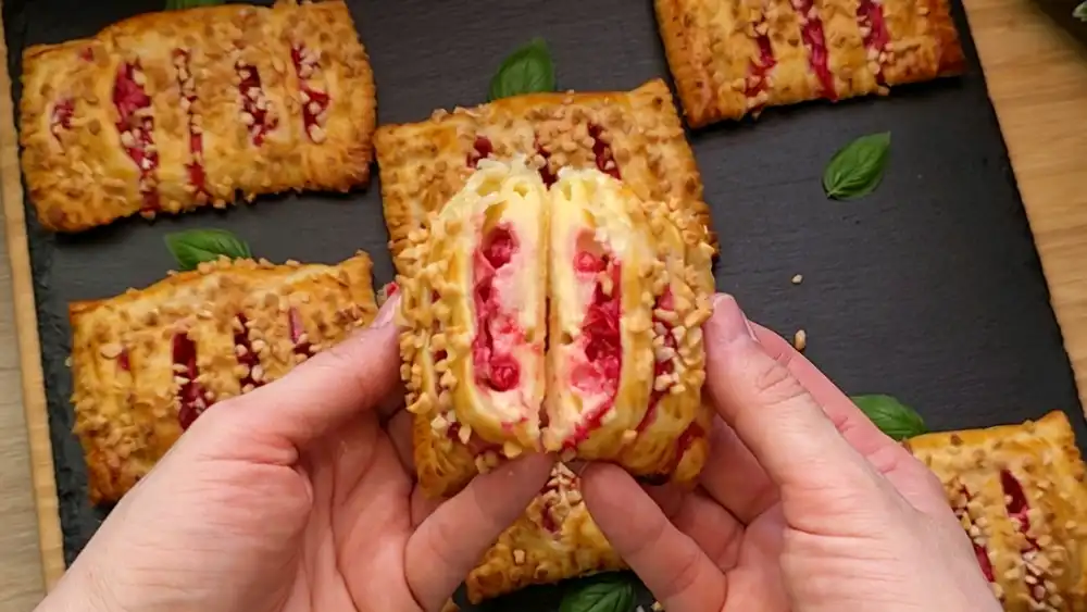 Detailansicht einer frisch gebackenen Quark-Tasche mit Fokus auf die gerösteten, gehackten Mandeln, den krossen Blätterteigrand und die saftigen roten Johannisbeeren in der Creme.