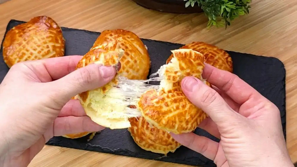 Detailansicht einer aufgeschnittenen, runden Käsetasche mit Fokus auf den geschmolzenen Käsekern, den cremigen Kräuterfrischkäse und die krosse Kruste.