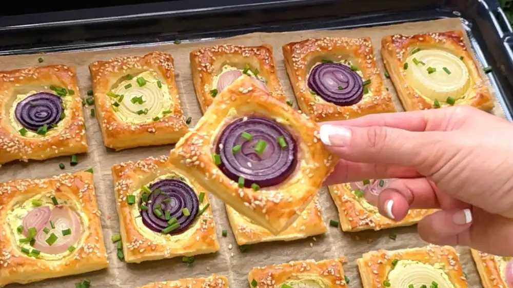 Detailansicht eines einzelnen Zwiebel-Häppchens mit Fokus auf die geschmolzene Frischkäseschicht, die weichen, leicht karamellisierten Zwiebelringe und den krossen Sesamrand.