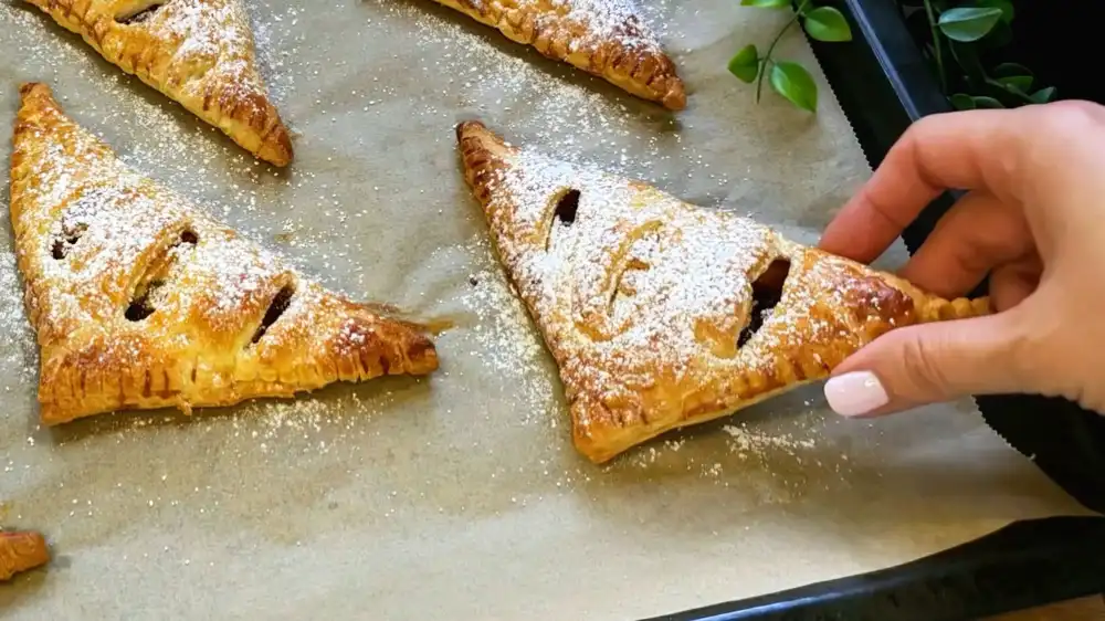 Detailansicht eines aufgeschnittenen Blätterteig-Dreiecks mit Fokus auf die lila Zwetschgenfüllung, geschmolzenes Marzipan und den krossen Gabelrand.