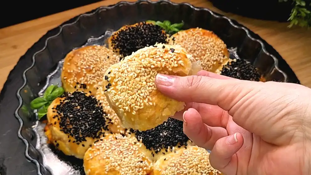 Detailansicht eines einzelnen, leicht flach gedrückten Pizza-Blätterteigbällchens mit Fokus auf die knusprige Sesamkruste und die saftige Füllung.
