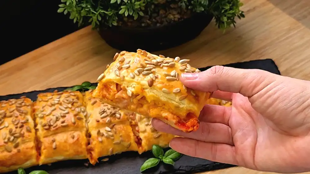 Detailansicht des angeschnittenen Pizza-Kissens mit Fokus auf den geschmolzenen Käse, Schinken, Mais und die krosse Blätterteigkruste.