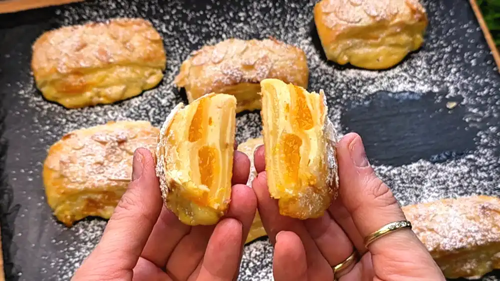 Detailansicht eines frisch gebackenen Quark-Mandarinen-Kissens aus Blätterteig mit Fokus auf die saftig gelben Mandarinenstücke und die kross gerösteten Mandelplättchen.